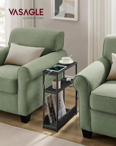 Slim three-tier side table with charging station between green armchairs, ideal for compact living spaces.