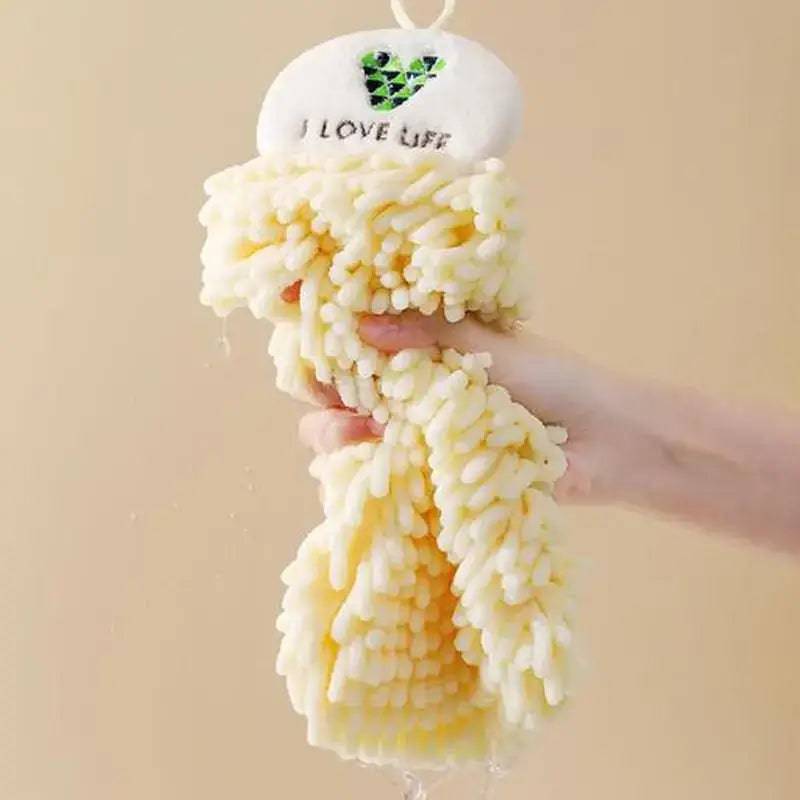 Hand squeezing a soft yellow chenille towel with 'I LOVE LIFE' embroidered, showcasing its absorbent texture.