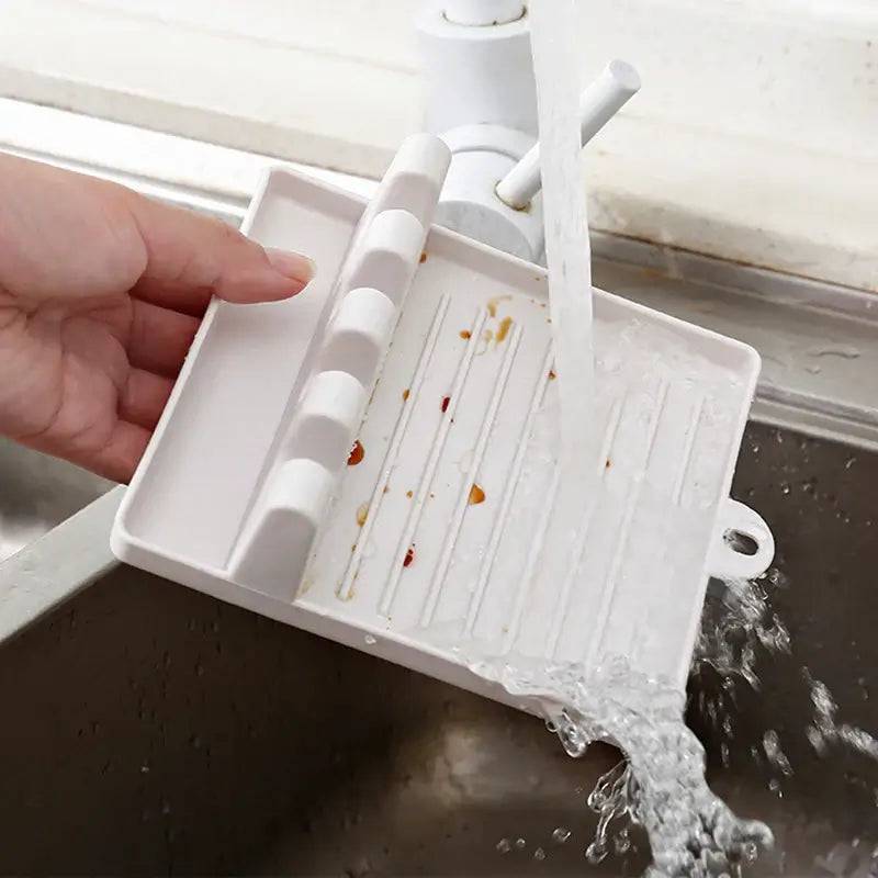 Hand holding a plastic sink strainer tray while water flows into it, showcasing its practical kitchen design.