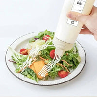 Hand pouring creamy sauce from a Multi-Purpose Condiment Dispenser onto a fresh salad.