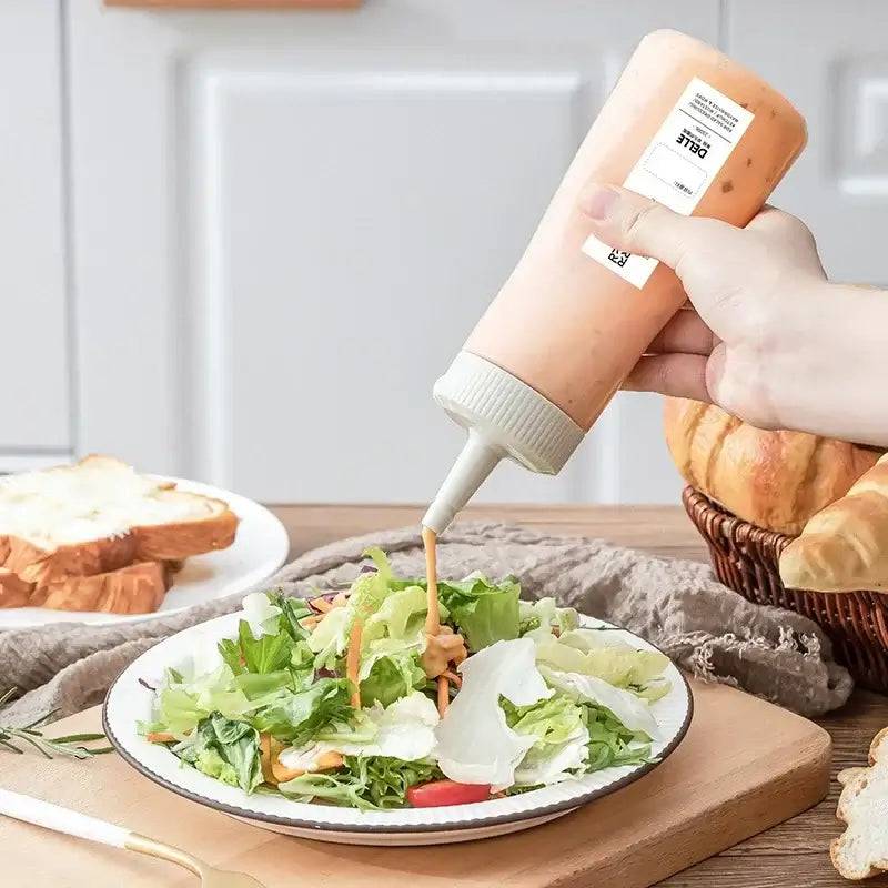 Person using a condiment dispenser to drizzle dressing on a fresh salad in a kitchen setting.