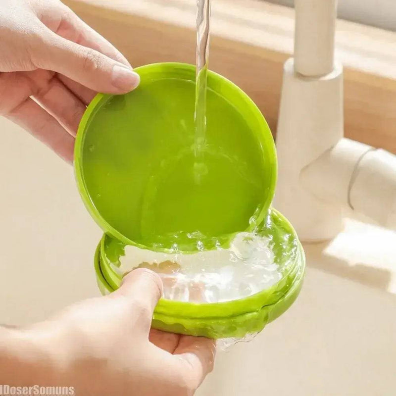 Hands holding a green silicone food storage container under running water, showcasing its easy-to-clean feature.