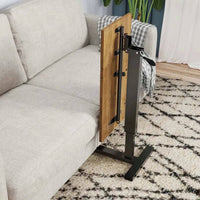 Adjustable overbed table with rolling wheels beside a sofa, featuring a wooden tabletop and sleek black base.