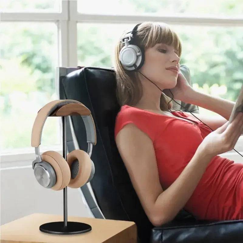 Woman enjoying music with headphones on a chair, featuring a walnut headphone stand in the foreground.