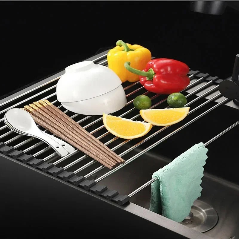Foldable stainless steel draining rack with colorful peppers, fruits, and utensils on a kitchen sink.