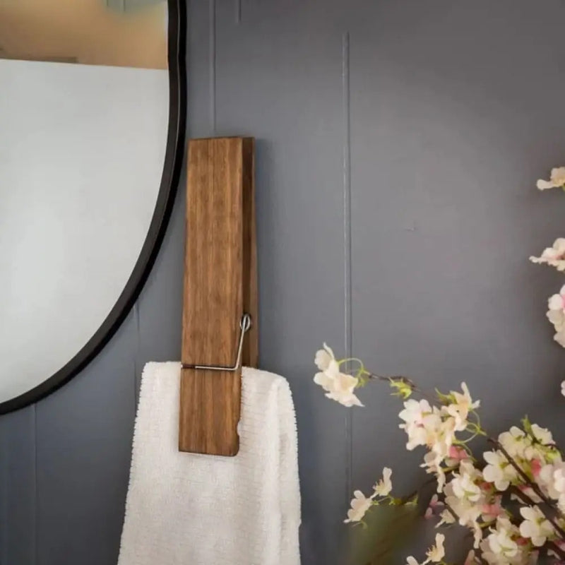 Giant wooden towel clip in rustic design holding a white towel against a grey wall, adding elegance to the space.
